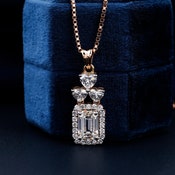 Pendant necklace with rose gold chain and rectangular halo pendant featuring clear rectangular and heart-shaped gemstones, front view on blue velvet display