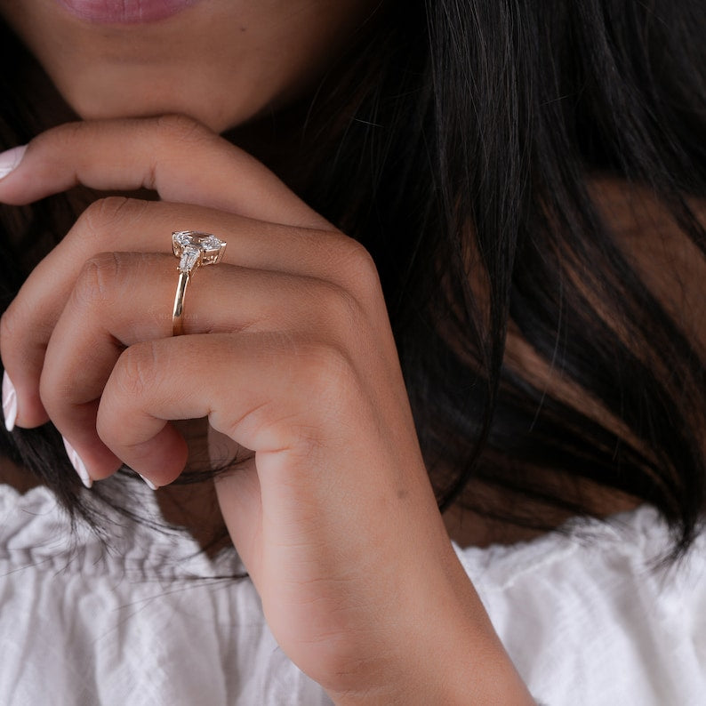 Engagement ring with gold-toned band, hexagon center stone, tapered baguette side stones, worn on hand, side profile view