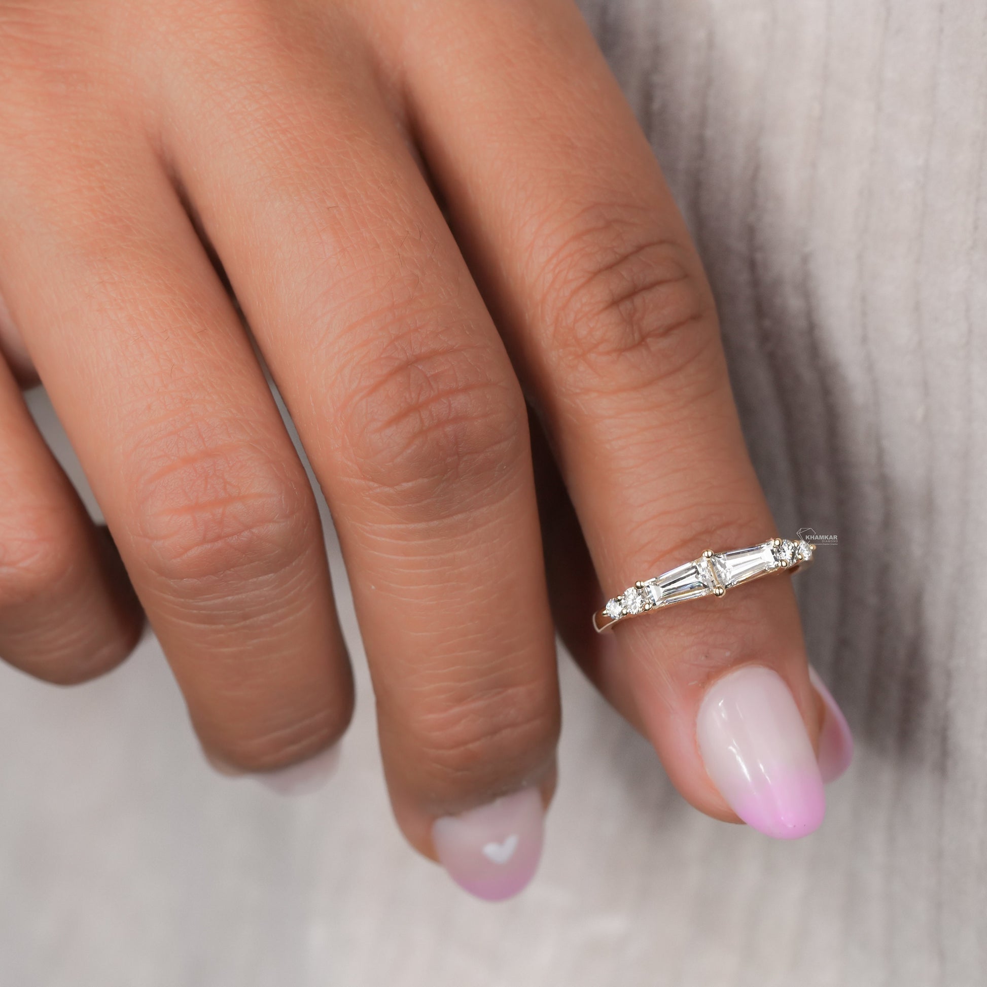 Engagement ring with yellow gold band, horizontal baguette-cut clear center gemstone and round side stones, worn on finger, angled top view
