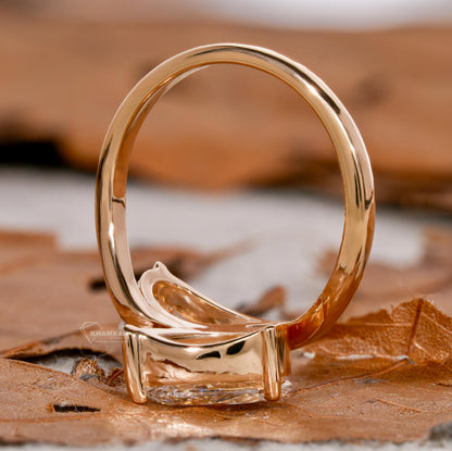 Engagement ring with yellow metal bypass band, two pear-shaped clear gemstones, rear profile view on leaf background
