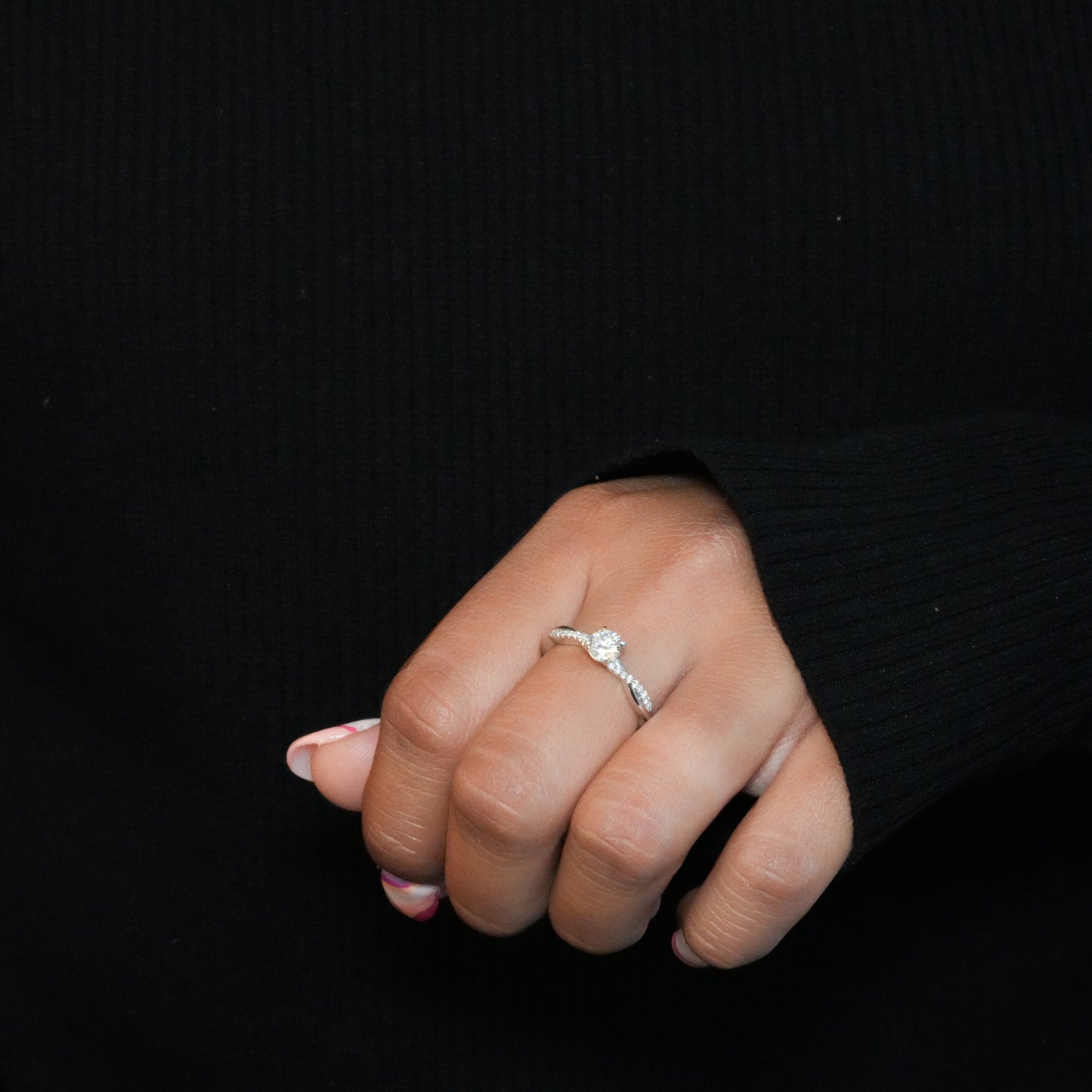 Ring with round clear center stone, twisted white metal band with pavé-set shoulders, worn on a hand, angled view
