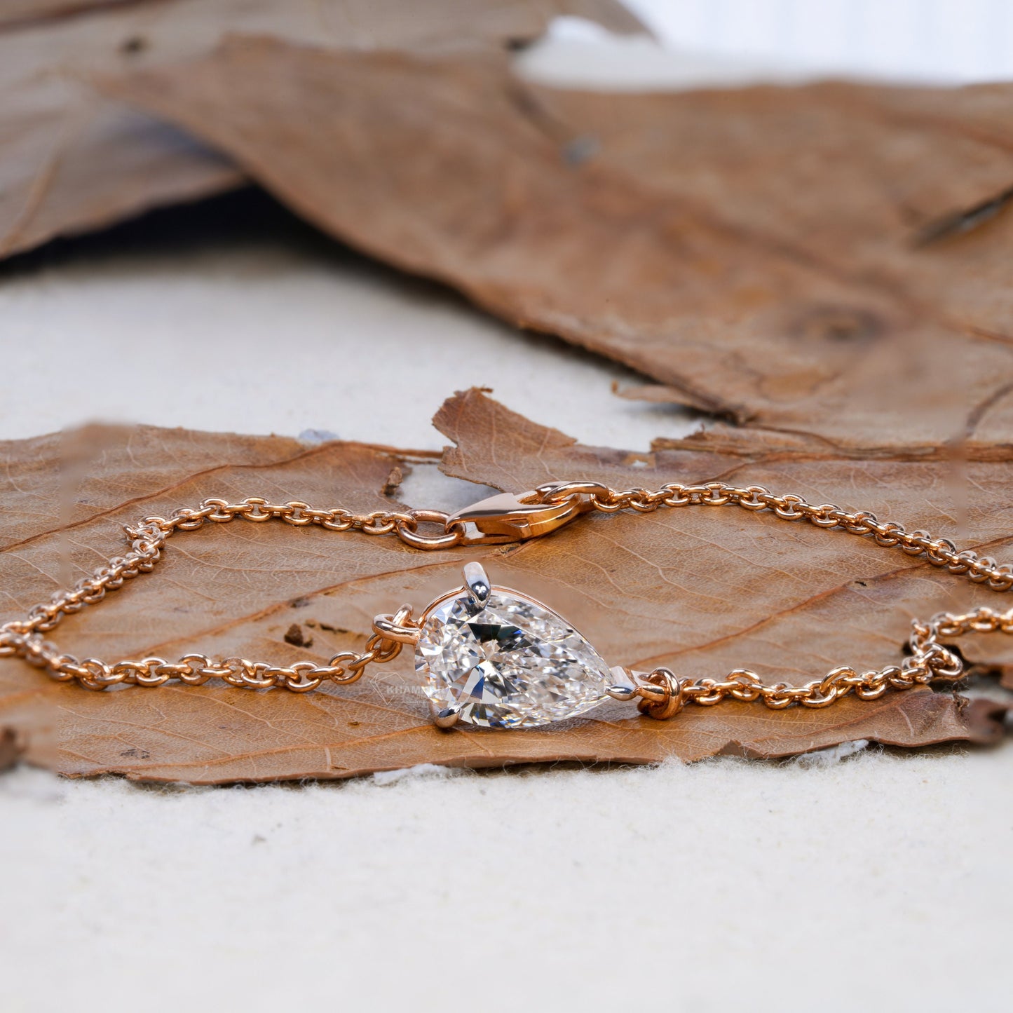 Bracelet with pear-shaped clear stone in yellow metal chain setting on dried leaf, angled close-up view, delicate chain bracelet jewelry
