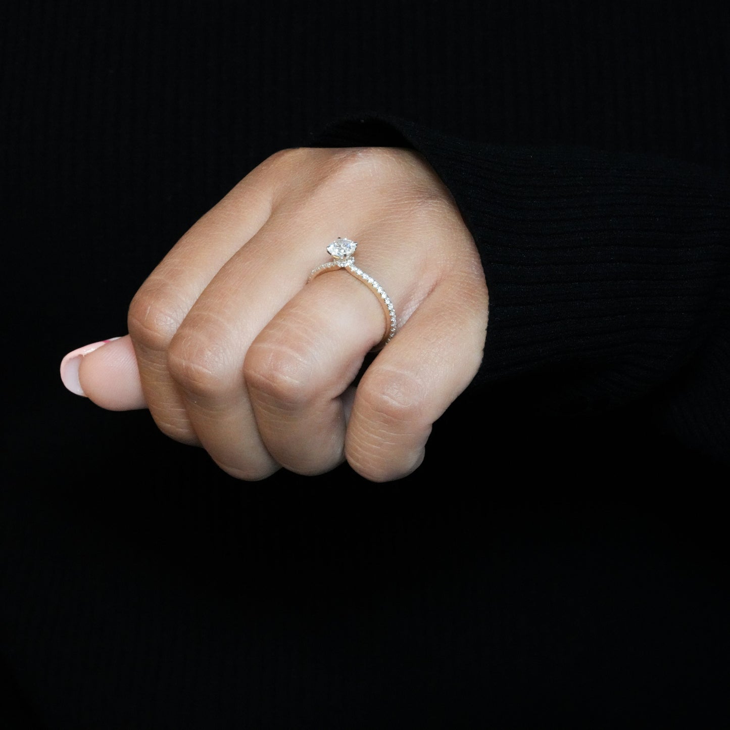 Engagement ring with round clear center stone, white metal pavé band, worn on hand, angled front view
