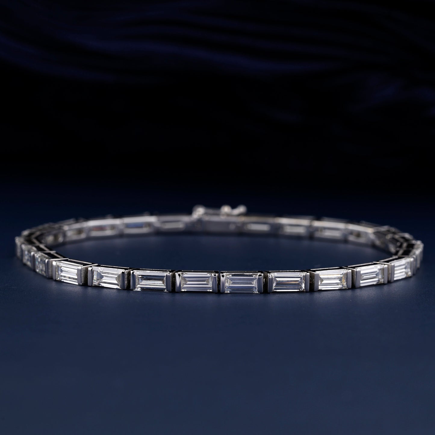 Bracelet with white metal links, rectangular step-cut stones in tennis bracelet design, oval display, angled front view on a dark background
