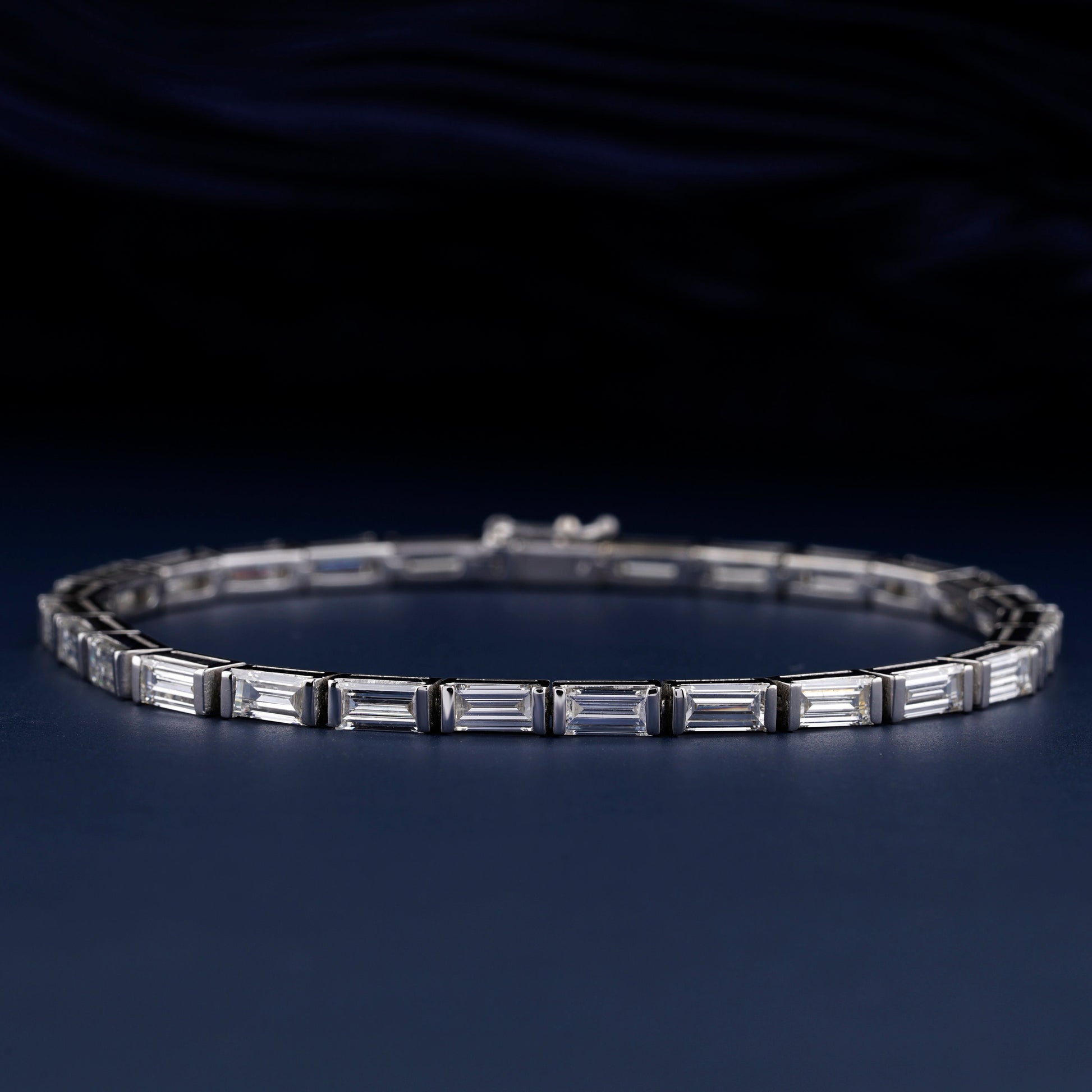 Bracelet with white metal links, rectangular step-cut stones in tennis bracelet design, oval display, angled front view on a dark background
