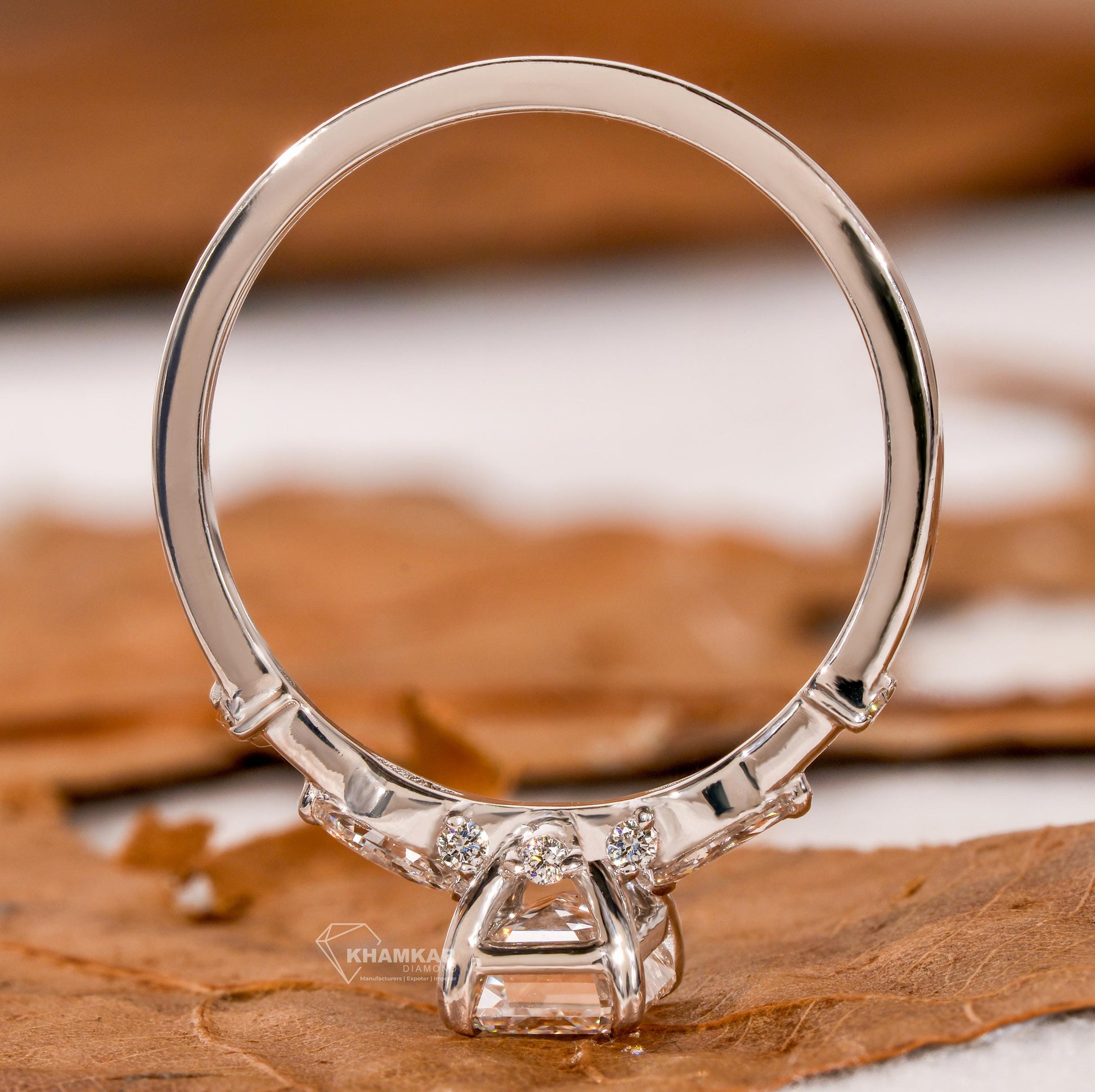Engagement ring with white metal band, emerald-cut clear center stone, open gallery setting and rear profile view
