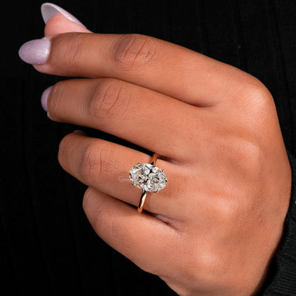 Engagement ring with yellow metal band, oval solitaire gemstone, worn on finger, angled top view
