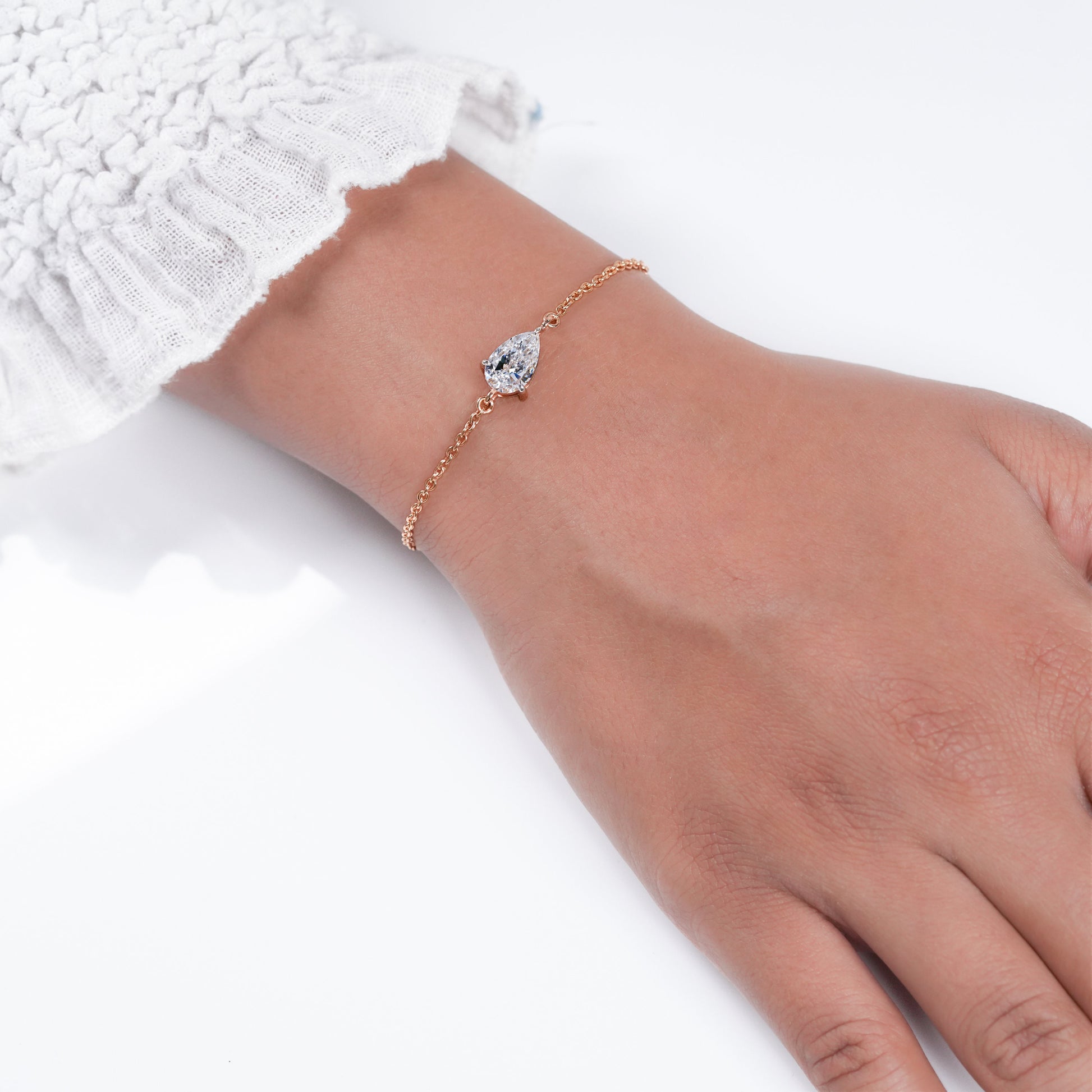 Bracelet with pear-shaped clear stone on yellow metal chain, worn on wrist, top view, delicate chain bracelet jewelry
