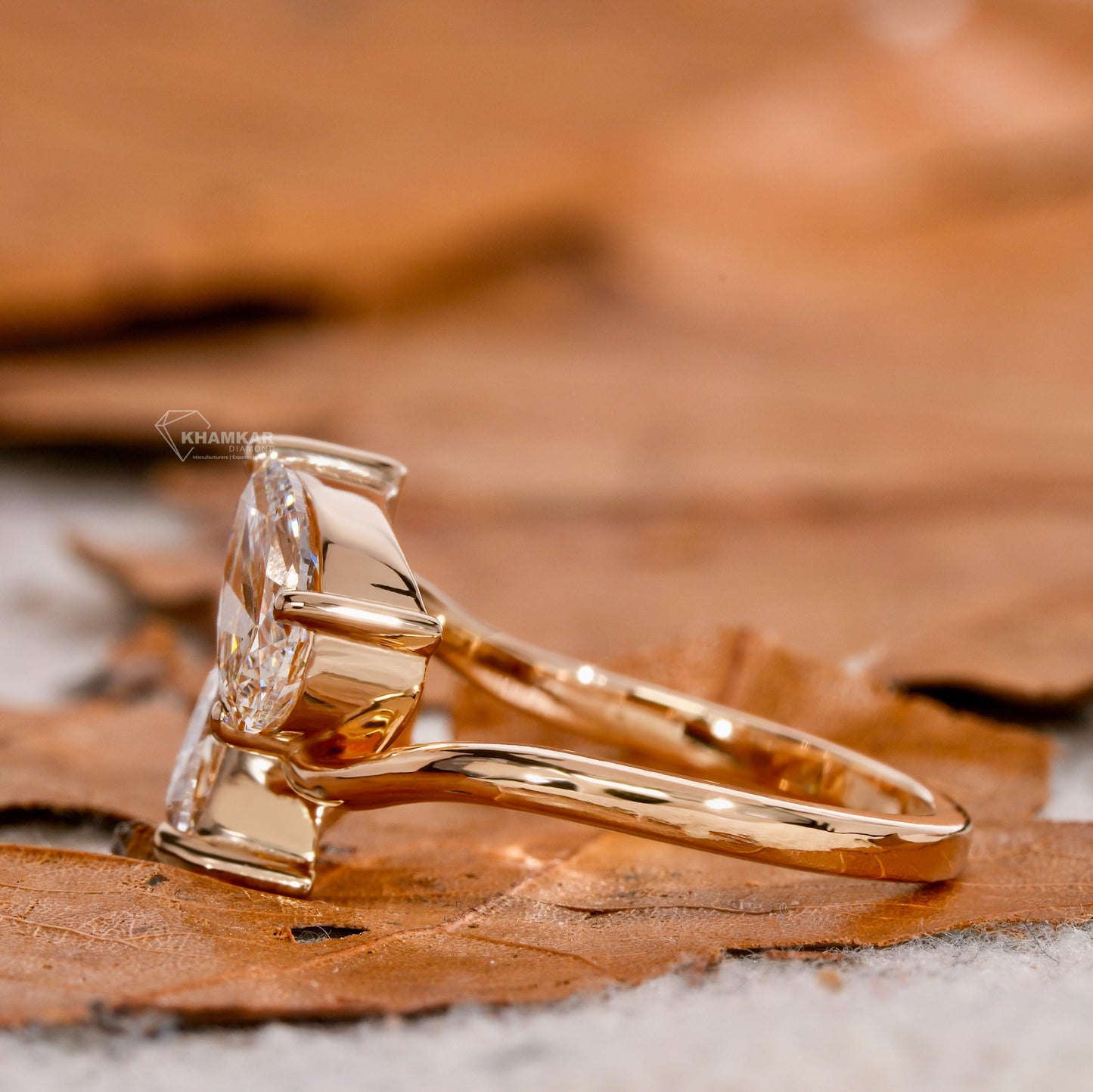 Engagement ring with yellow metal bypass band, two pear-shaped clear gemstones, side profile view on leaf background

