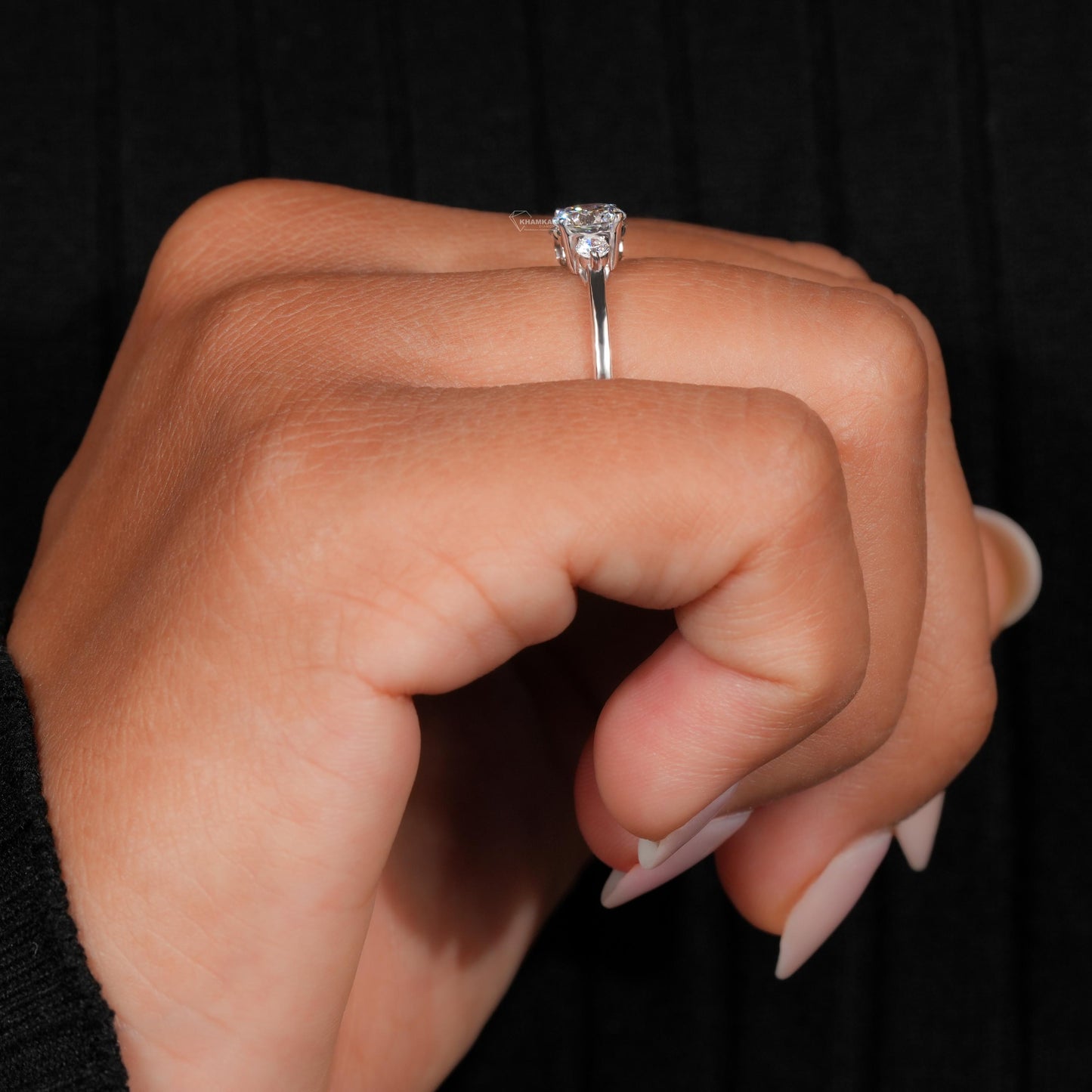 Ring silver-tone band with raised oval clear center stone and small side stones, side profile view on finger