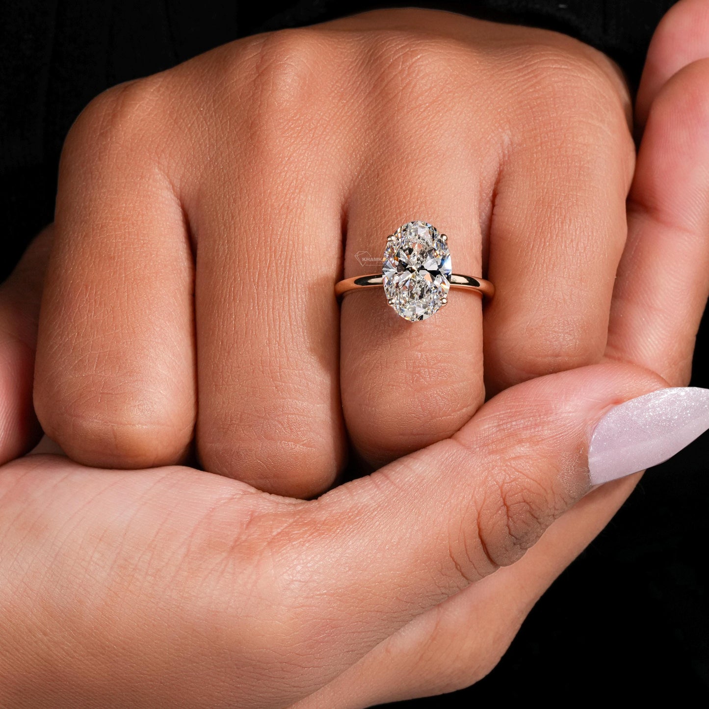 Engagement ring with yellow metal band, oval solitaire gemstone, worn on finger, top view
