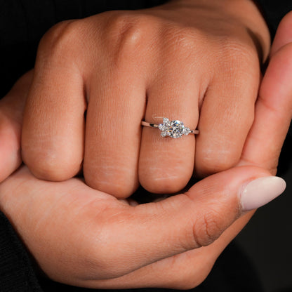 Engagement ring with white metal, round center stone, round accent diamond cluster setting, worn on finger, front view
