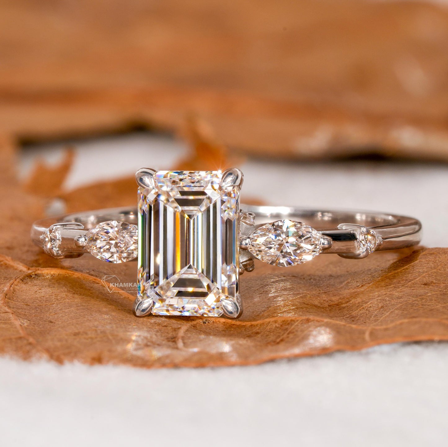 Engagement ring with white metal band, emerald-cut clear center stone, marquise side stones and round accents, front view
