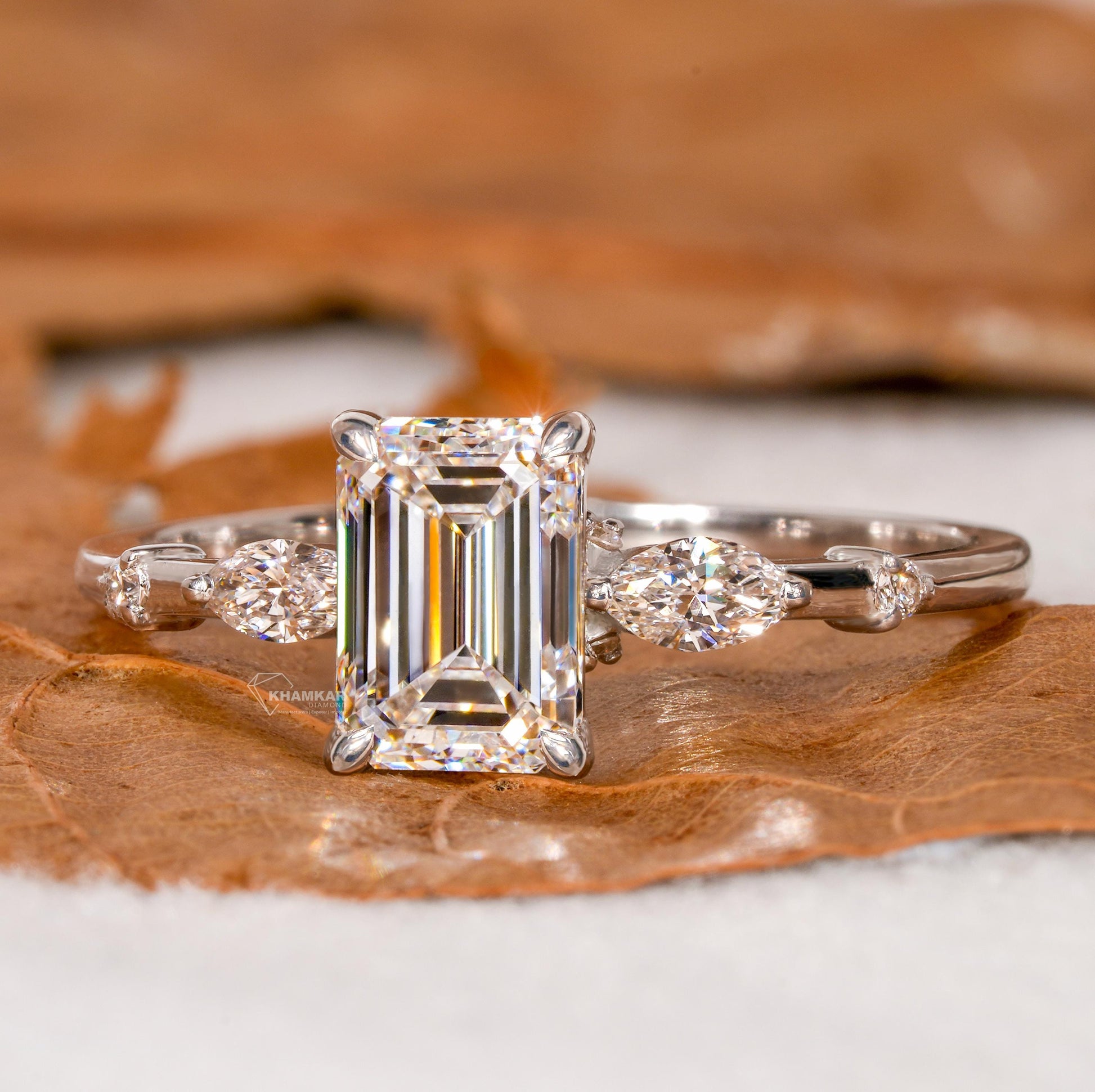 Engagement ring with white metal band, emerald-cut clear center stone, marquise side stones and round accents, front view
