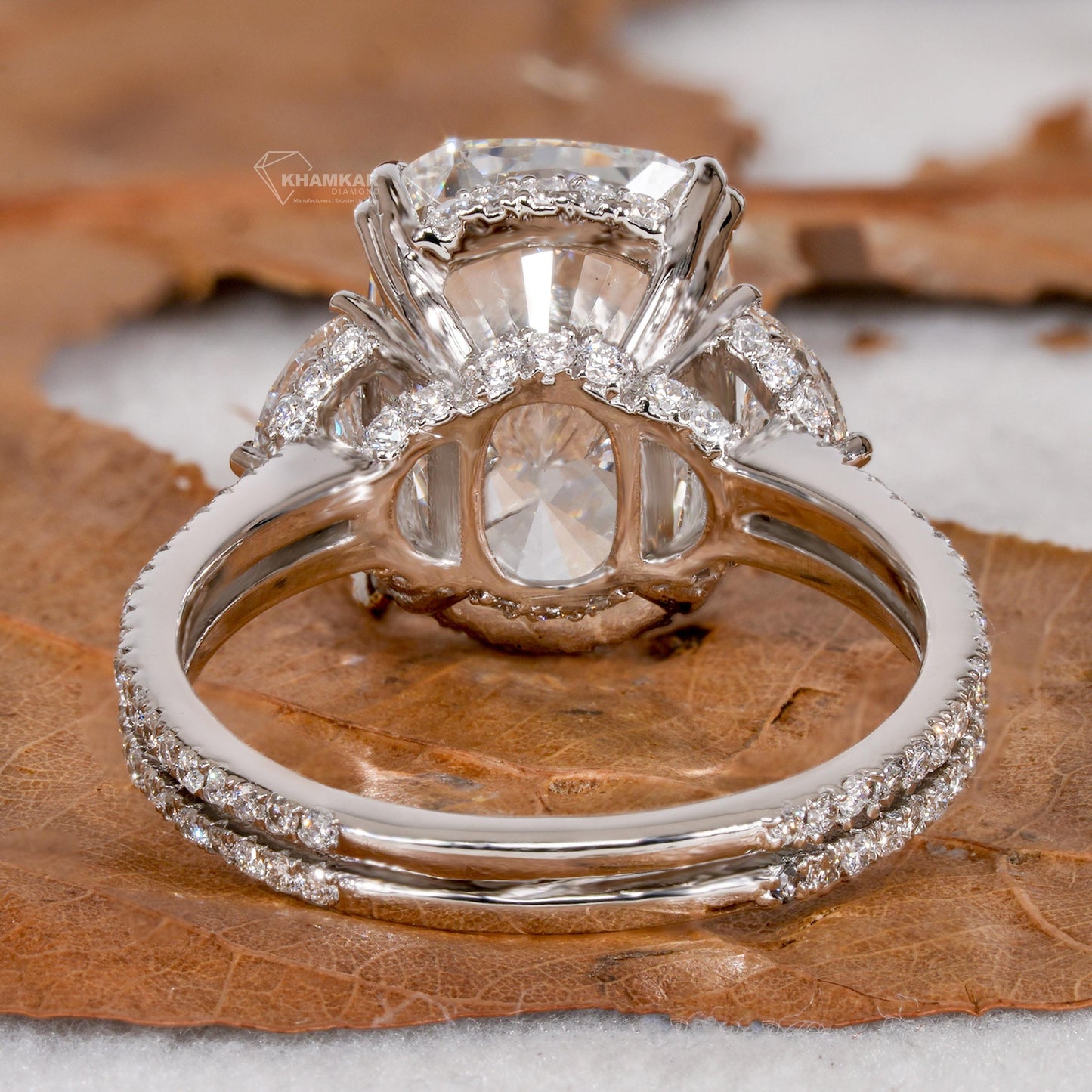 Engagement ring with white metal split shank, elongated cushion-cut clear center stone, oval side stones, open gallery, rear view
