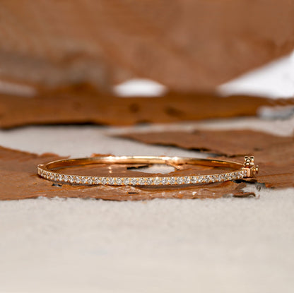 Bracelet with yellow metal band, round stones in a slim tennis bracelet design, side profile view on a textured surface
