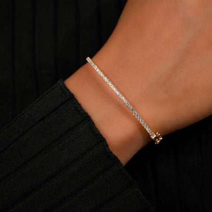 Bracelet with yellow metal band, slim round stone tennis design, worn on wrist, close-up angled side view against a black sleeve background
