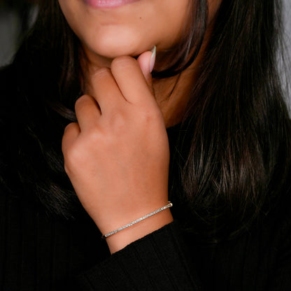 Bracelet with yellow metal band, slim round stone tennis design, worn on wrist with hand near face, angled front view against a black top background
