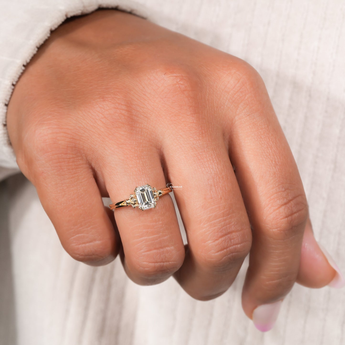 Engagement ring with rectangular clear gemstone, yellow metal band, floral-inspired side accent stones, worn on finger, angled view
