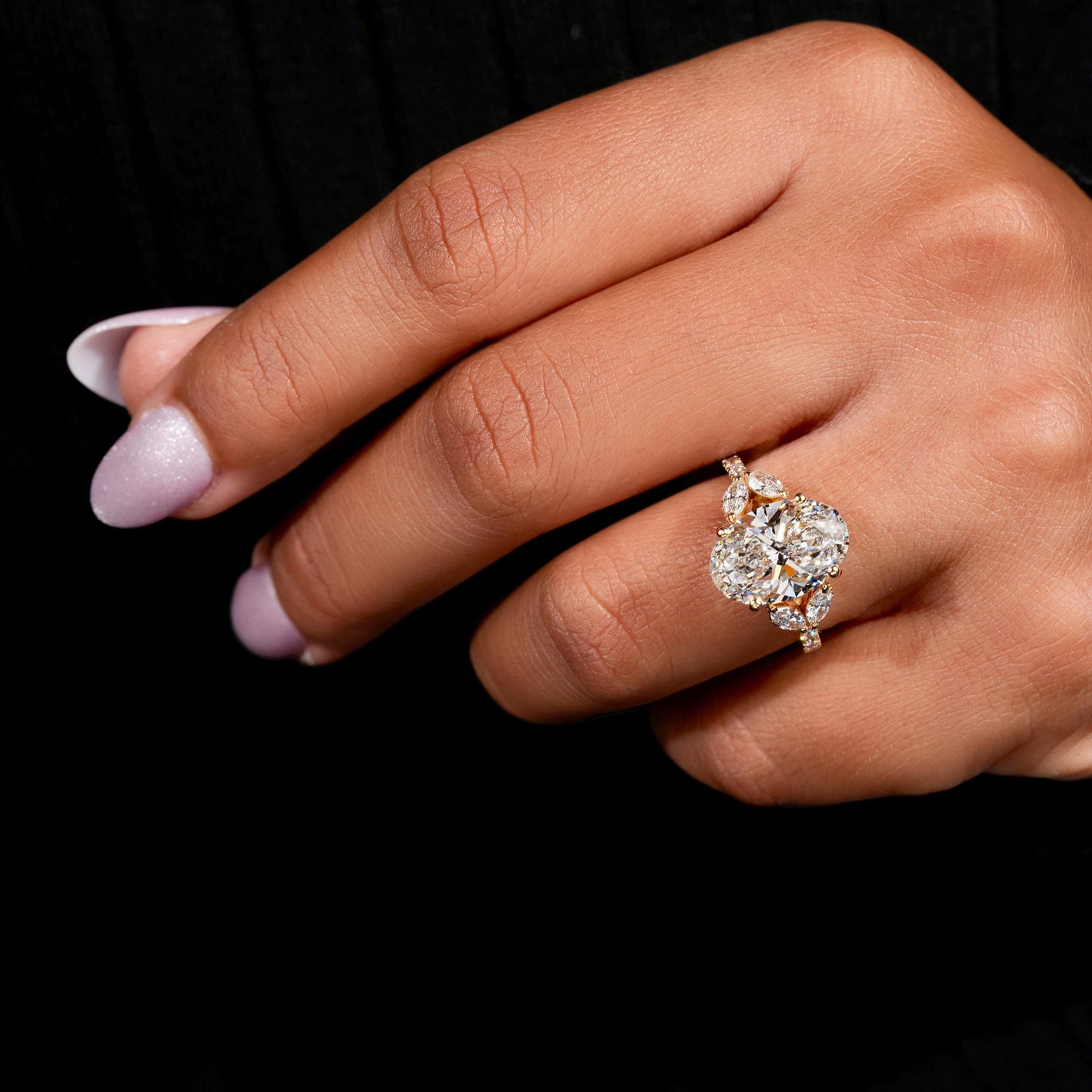 Engagement ring with yellow gold band, oval clear center gemstone, marquise side stones, worn on finger, angled hand view
