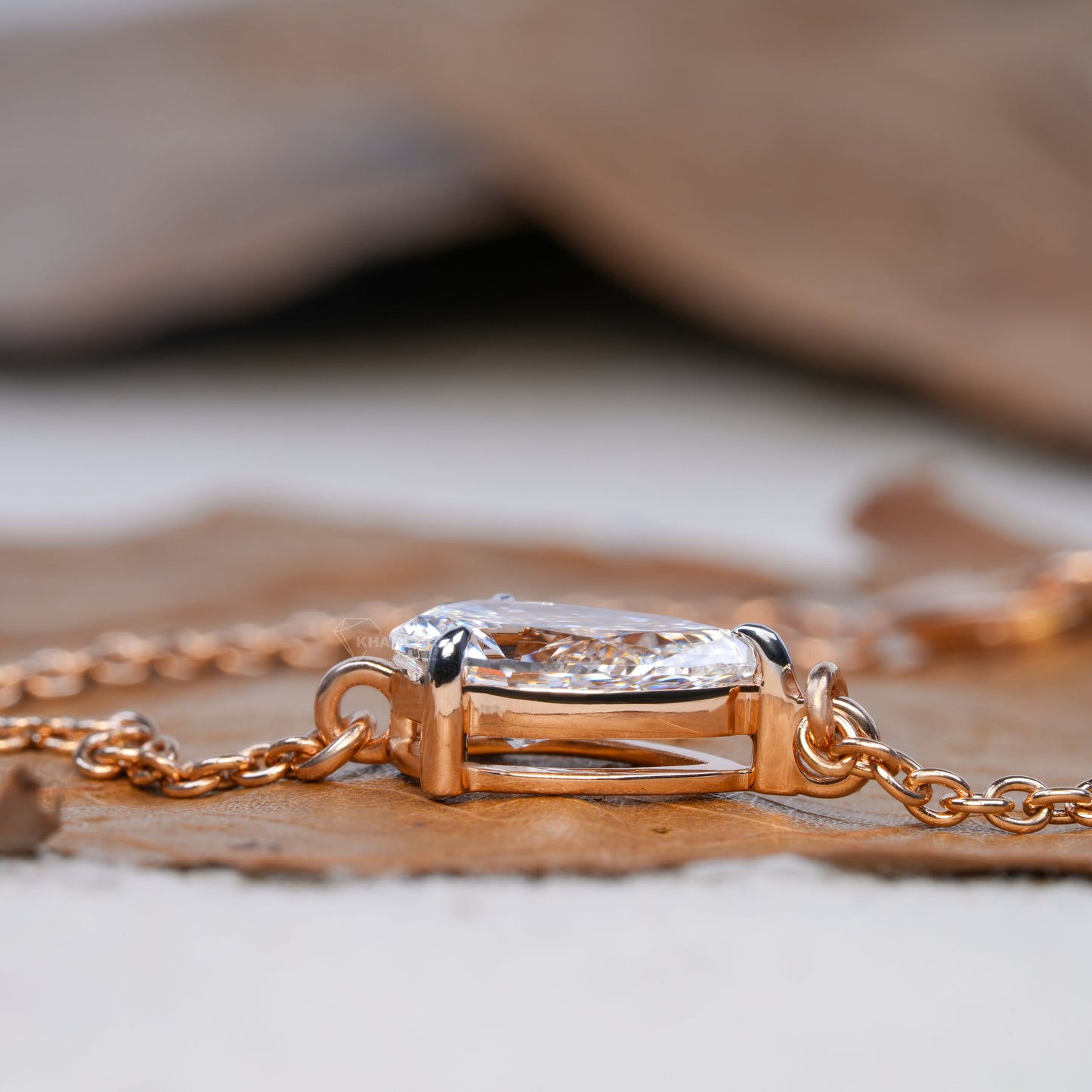 Bracelet with pear-shaped clear stone in yellow metal open setting, side profile close-up on dried leaf, delicate chain bracelet jewelry
