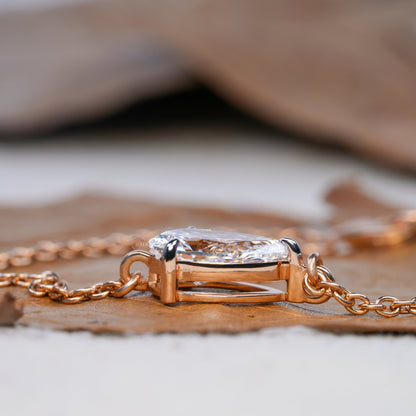 Bracelet with pear-shaped clear stone in yellow metal open setting, side profile close-up on dried leaf, delicate chain bracelet jewelry
