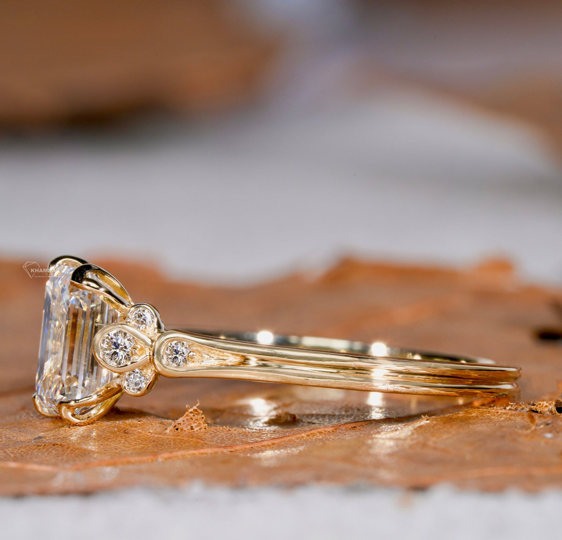 Engagement ring with rectangular clear gemstone, yellow metal band, floral-inspired round accent stones, side profile view
