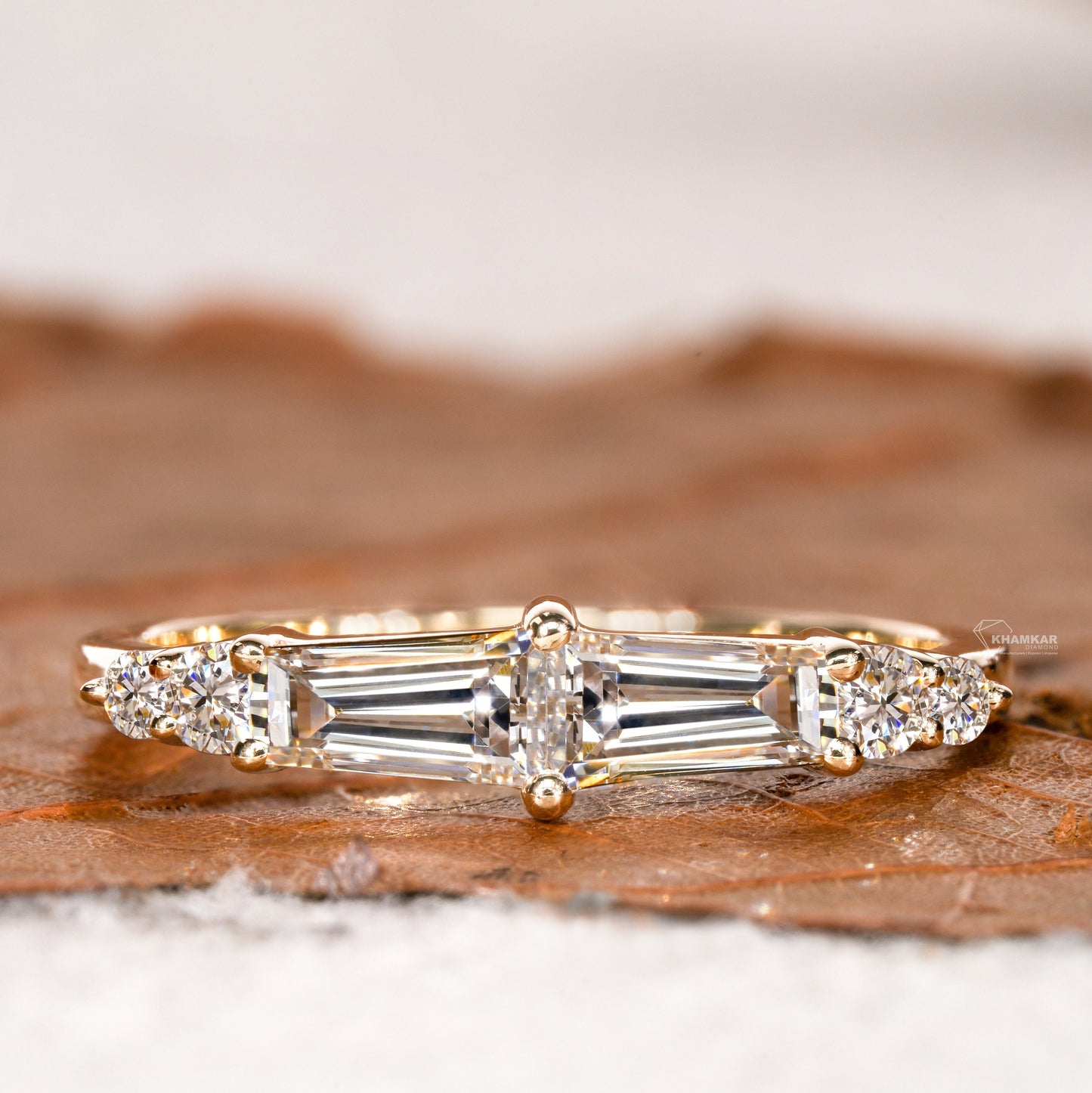 Engagement ring with rose gold band, horizontal baguette-cut clear center gemstone and round side stones, front view
