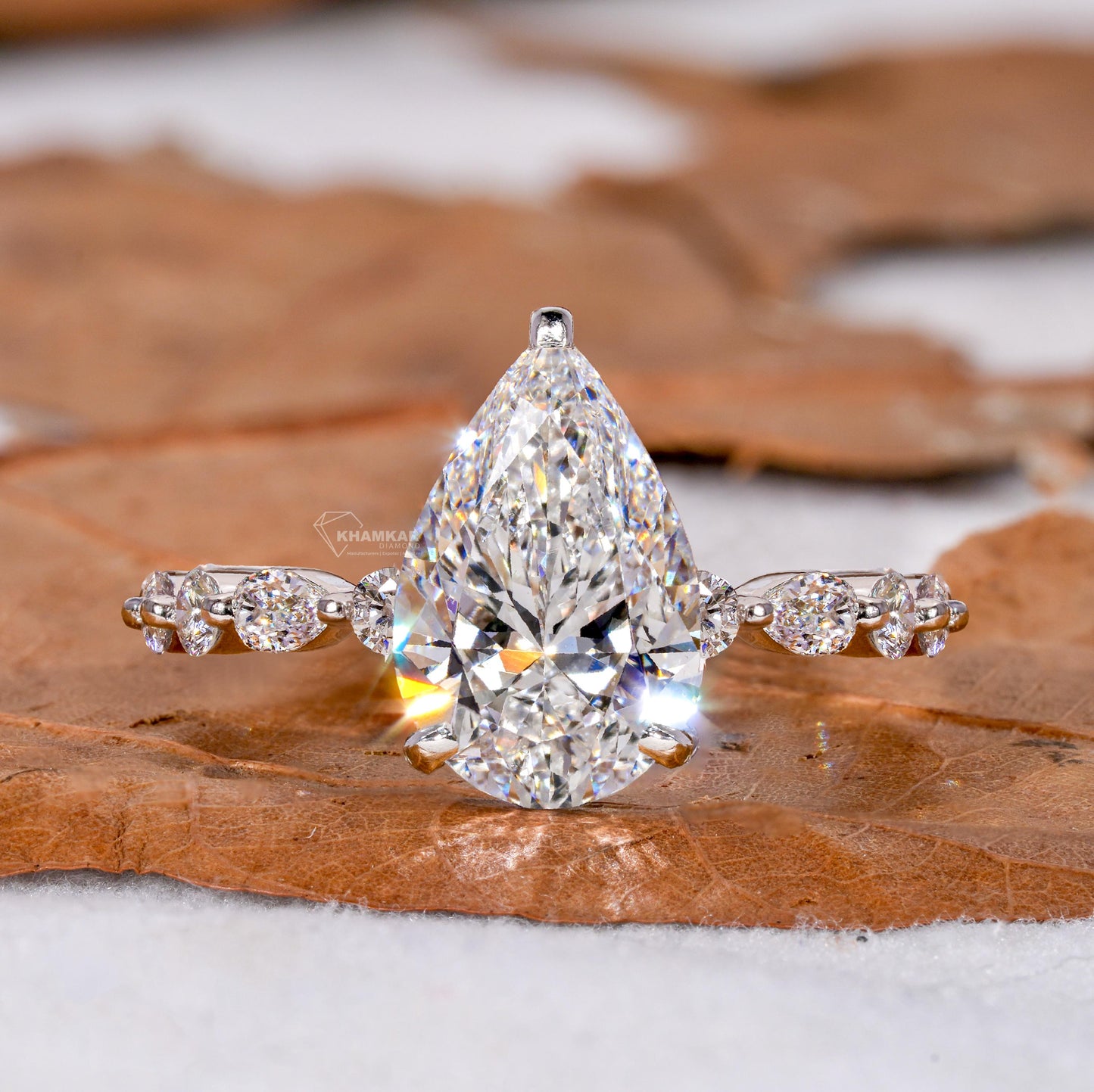 Engagement ring with polished white metal band, pear-shaped clear gemstone and round accent stones, front view
