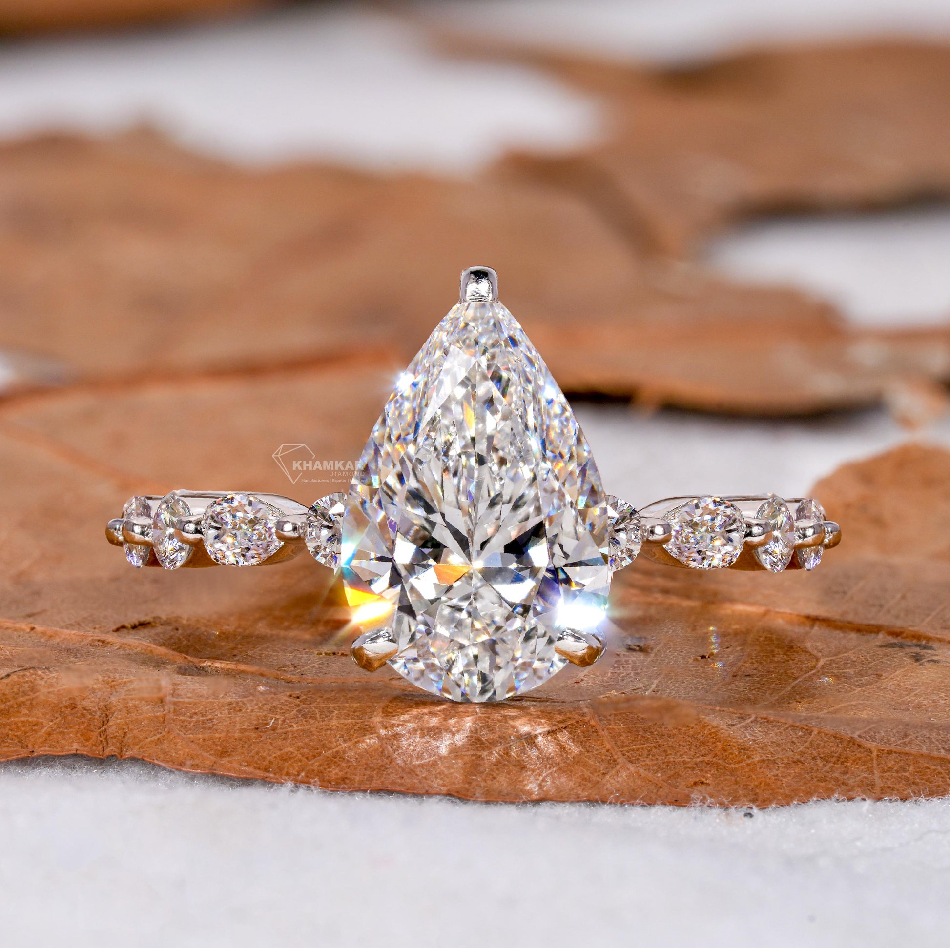 Engagement ring with polished white metal band, pear-shaped clear gemstone and round accent stones, front view
