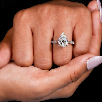 Engagement ring with polished white metal band, pear-shaped clear gemstone and round accent stones, worn on finger, front view
