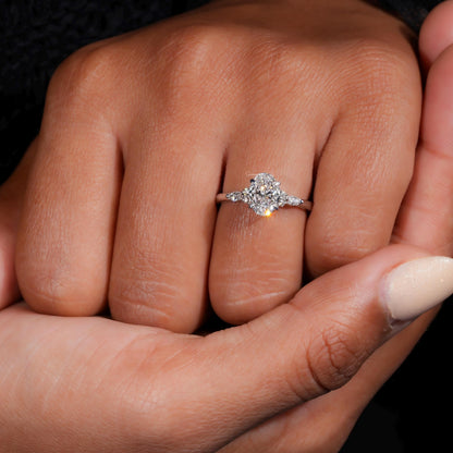 Engagement ring with oval clear center gemstone, polished white metal band, accent side stones and front view worn on finger
