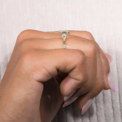 Engagement ring with yellow metal band, rectangular clear gemstone, floral-inspired gallery, worn on finger, side profile view
