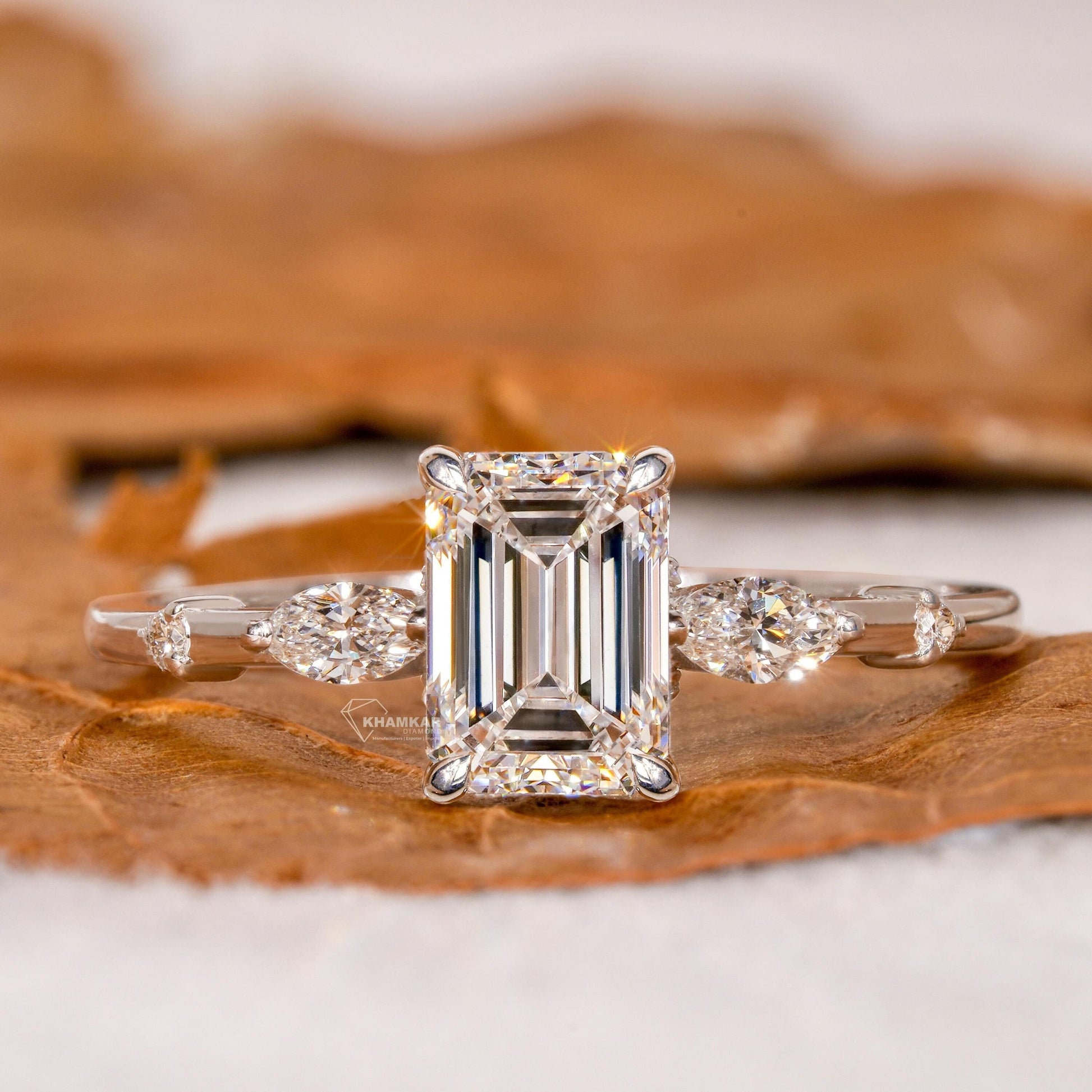 Engagement ring with white metal band, emerald-cut clear center stone, marquise side stones and round accents, front view
