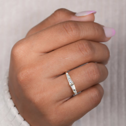 Engagement ring with white metal band, vertical baguette-cut clear center gemstone and round side stones, worn on finger, angled top view
