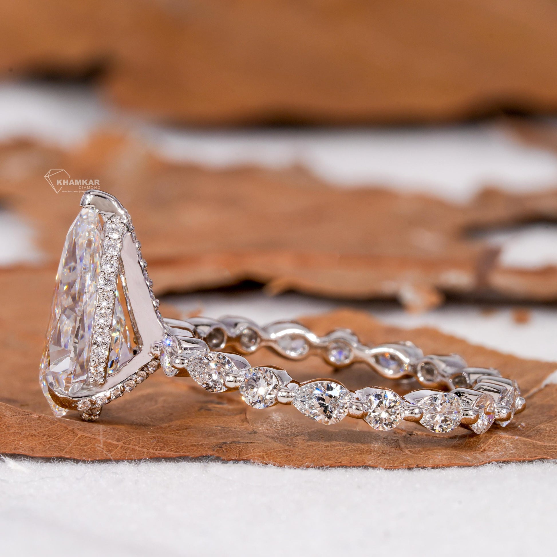 Engagement ring with polished white metal band, pear-shaped clear gemstone, halo setting and pear accent stones, side profile view
