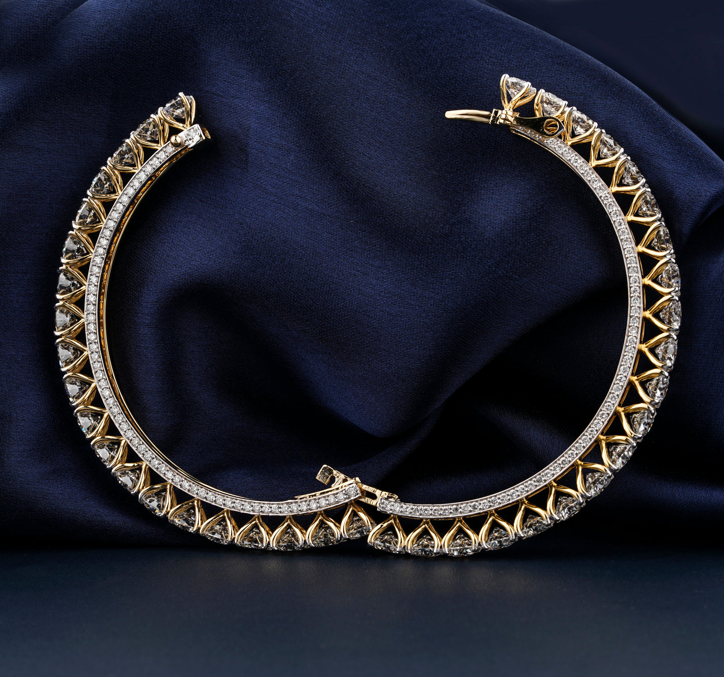 Bracelet with yellow metal band, heart-shaped stone design and pavé edge, open clasp detail, front view on dark blue fabric background

