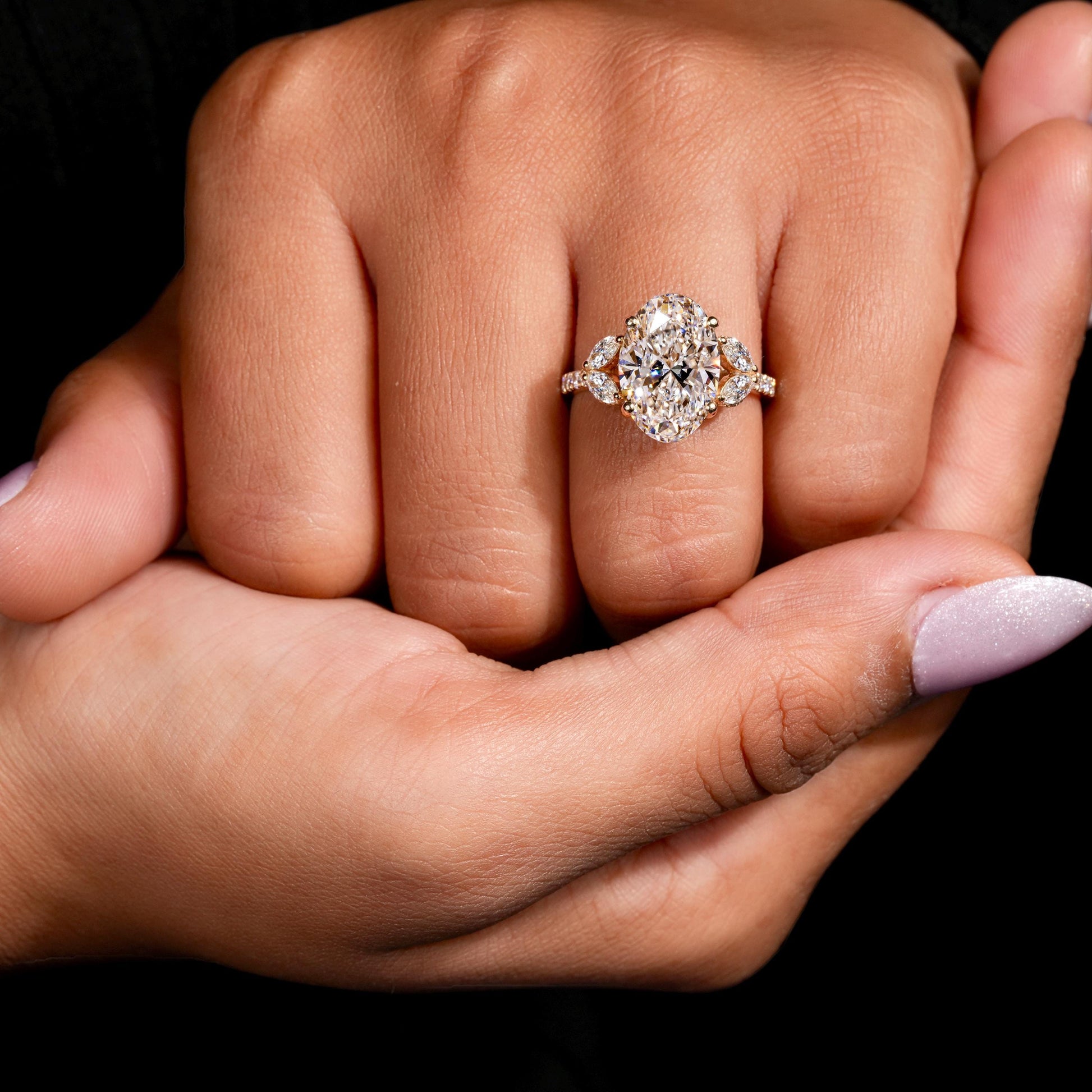 Engagement ring with yellow gold band, oval clear center gemstone, marquise side stones, worn on finger, top view
