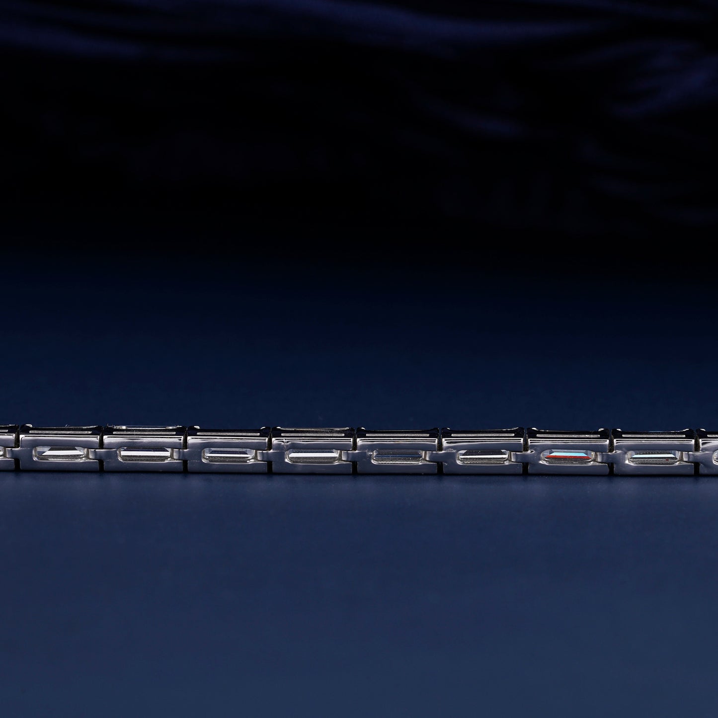 Bracelet with white metal links, rectangular step-cut stones in tennis bracelet design, close-up rear detail view on a dark background
