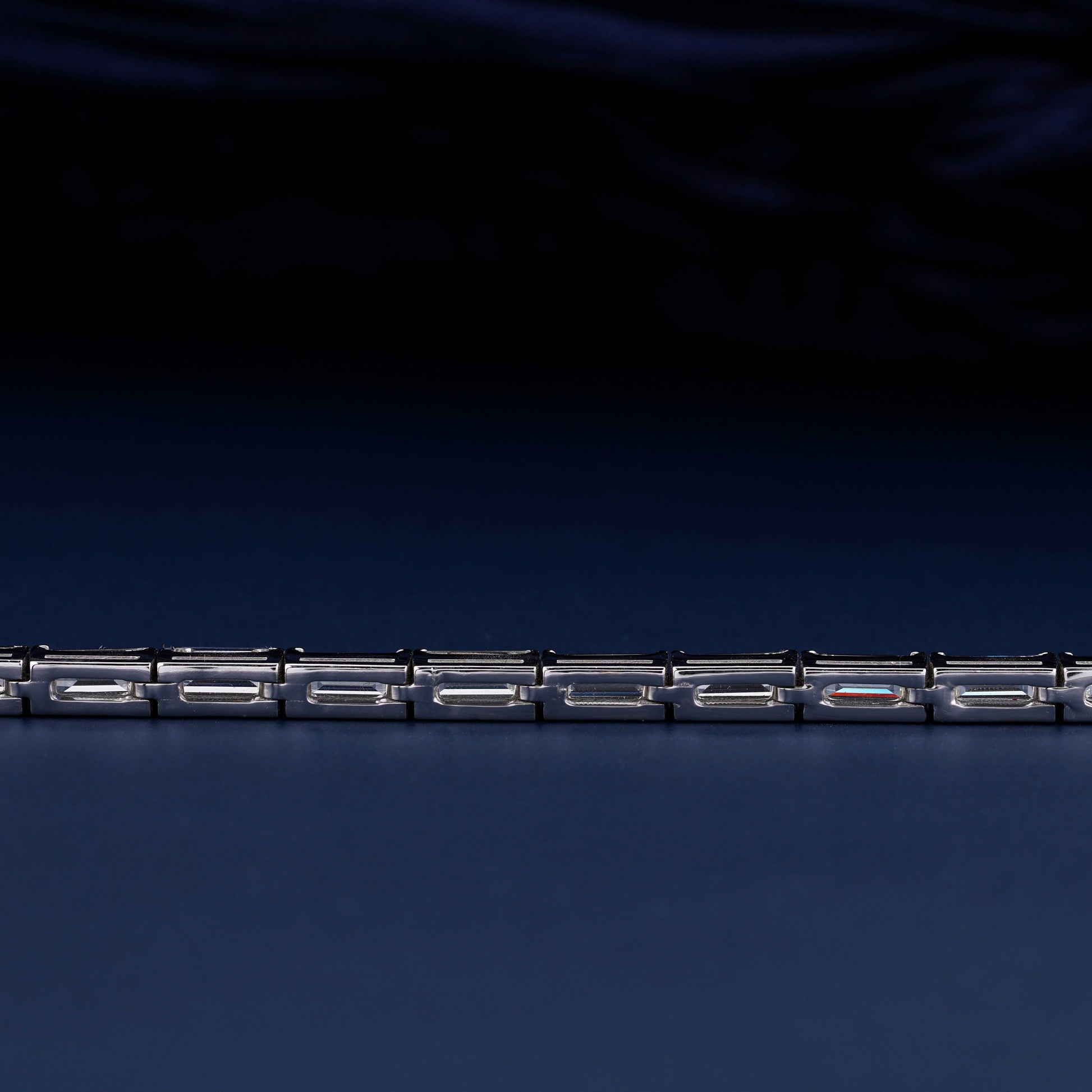 Bracelet with white metal links, rectangular step-cut stones in tennis bracelet design, close-up rear detail view on a dark background
