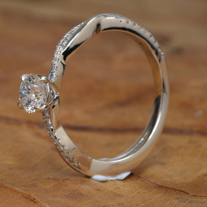 Ring with round clear solitaire, white metal twisted band, pavé-set shoulders, side profile on wooden surface
