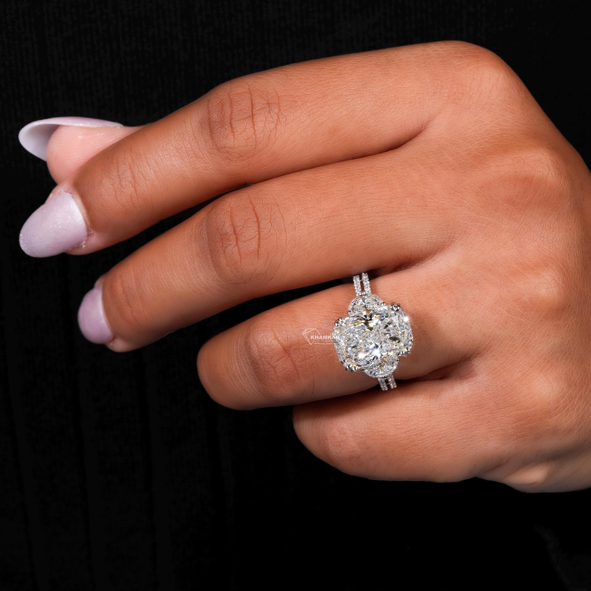 Engagement ring with white metal split shank, elongated cushion-cut clear center stone, oval side stones, worn on finger, angled view
