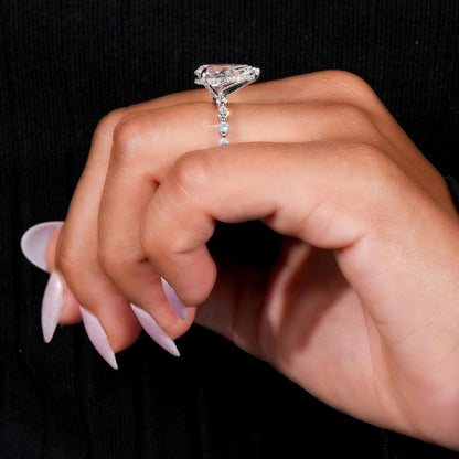 Engagement ring with polished white metal band, pear-shaped clear gemstone, raised basket setting and side profile, worn on finger
