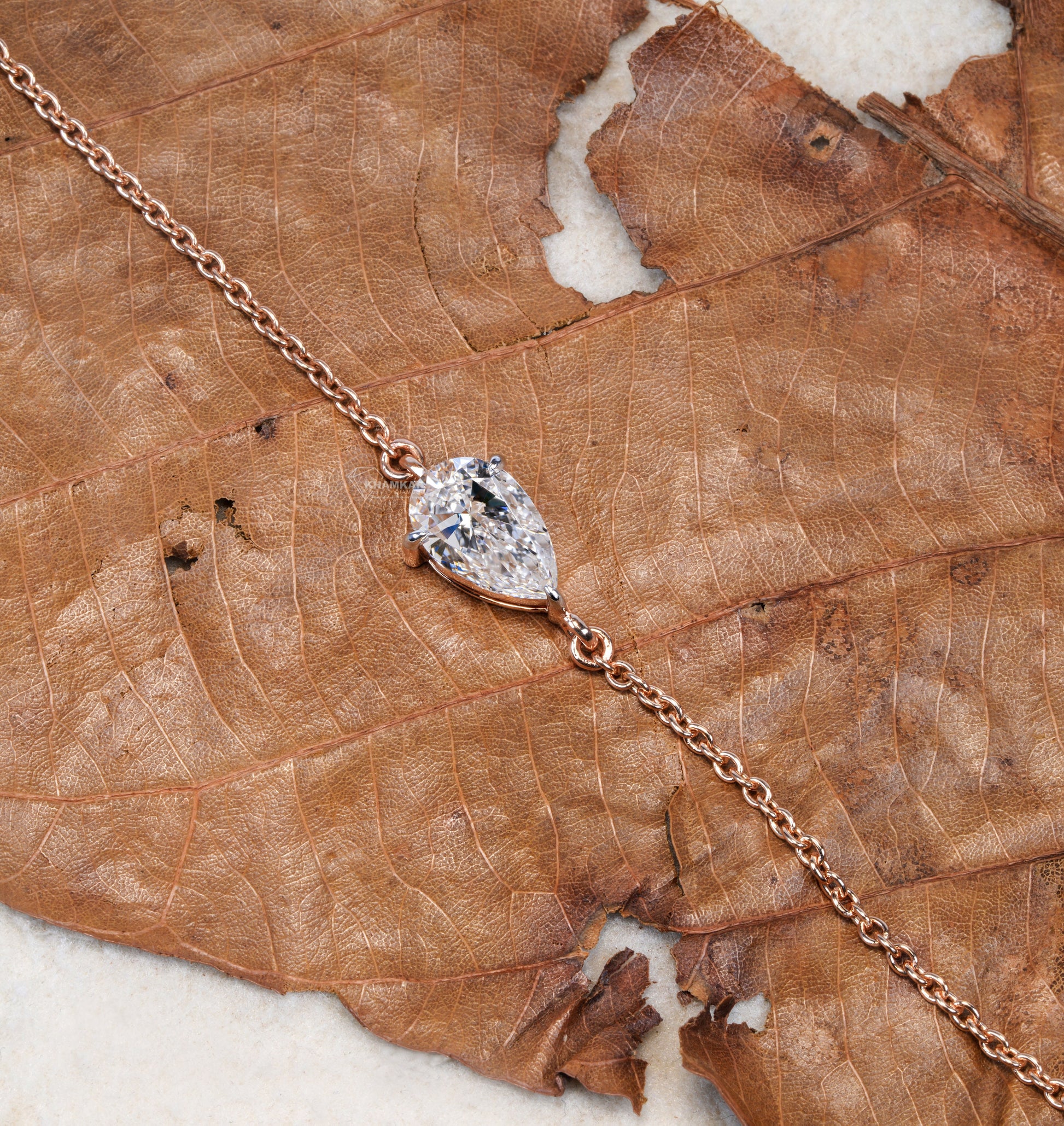 Bracelet with pear-shaped clear stone in yellow metal chain setting on dried leaf, top view, delicate chain bracelet jewelry
