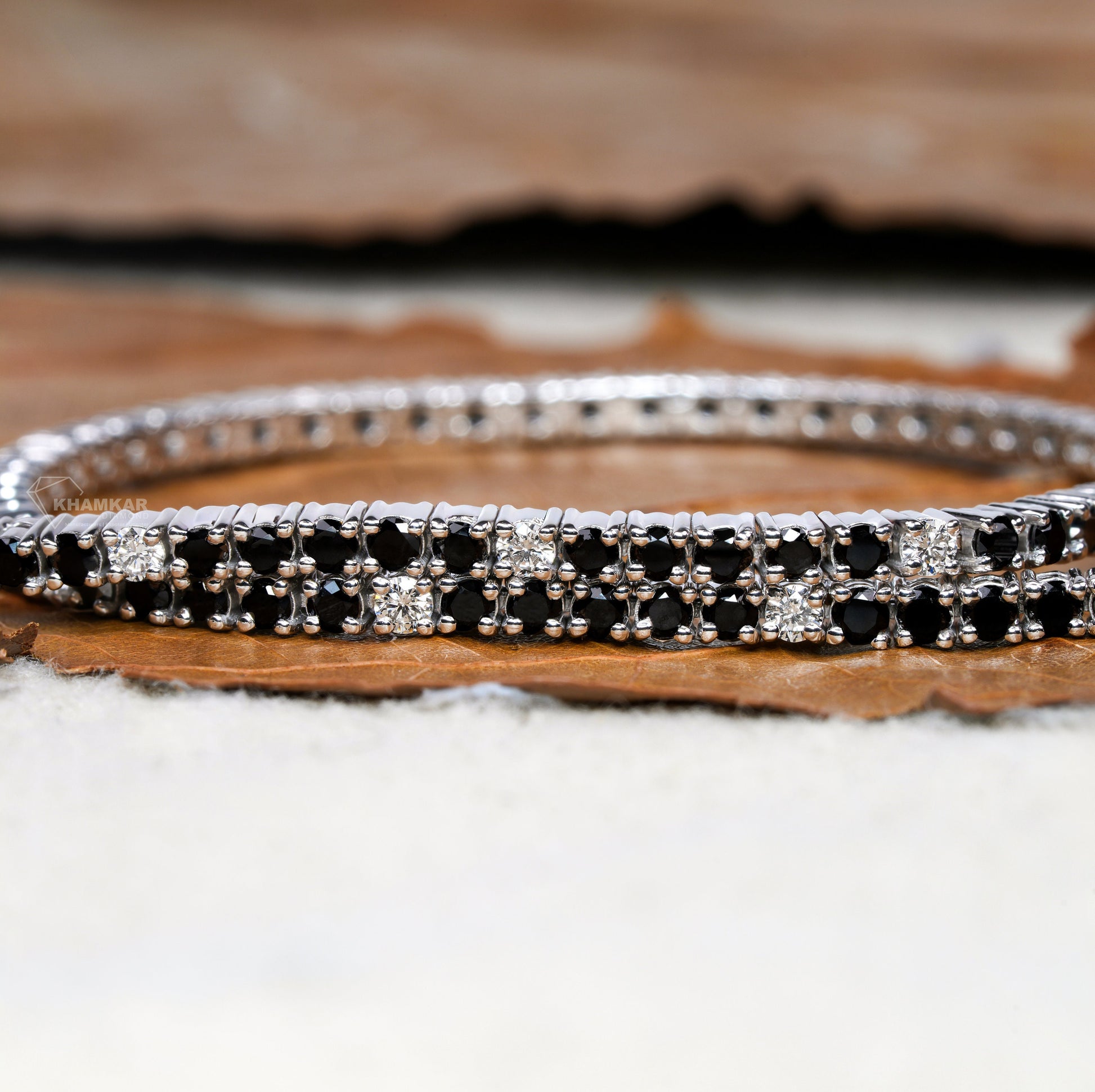 Bracelet with alternating black and clear round stones in a double-row white metal setting, close-up front view, tennis bracelet jewelry
