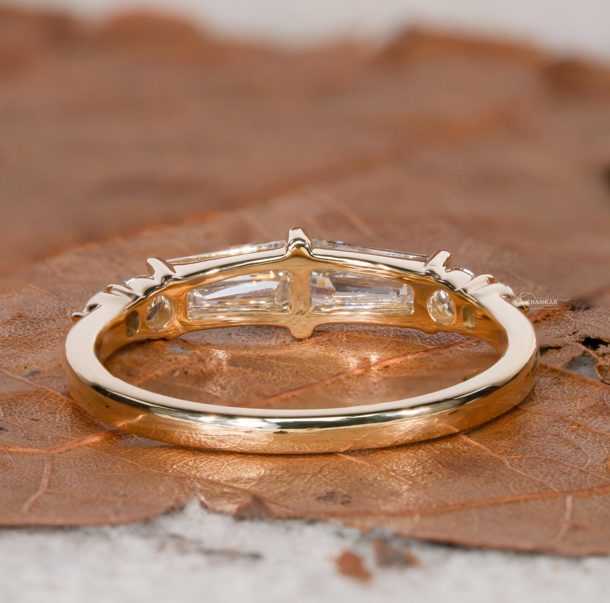 Engagement ring with yellow gold band, horizontal baguette-cut clear center gemstone in open gallery setting, rear view
