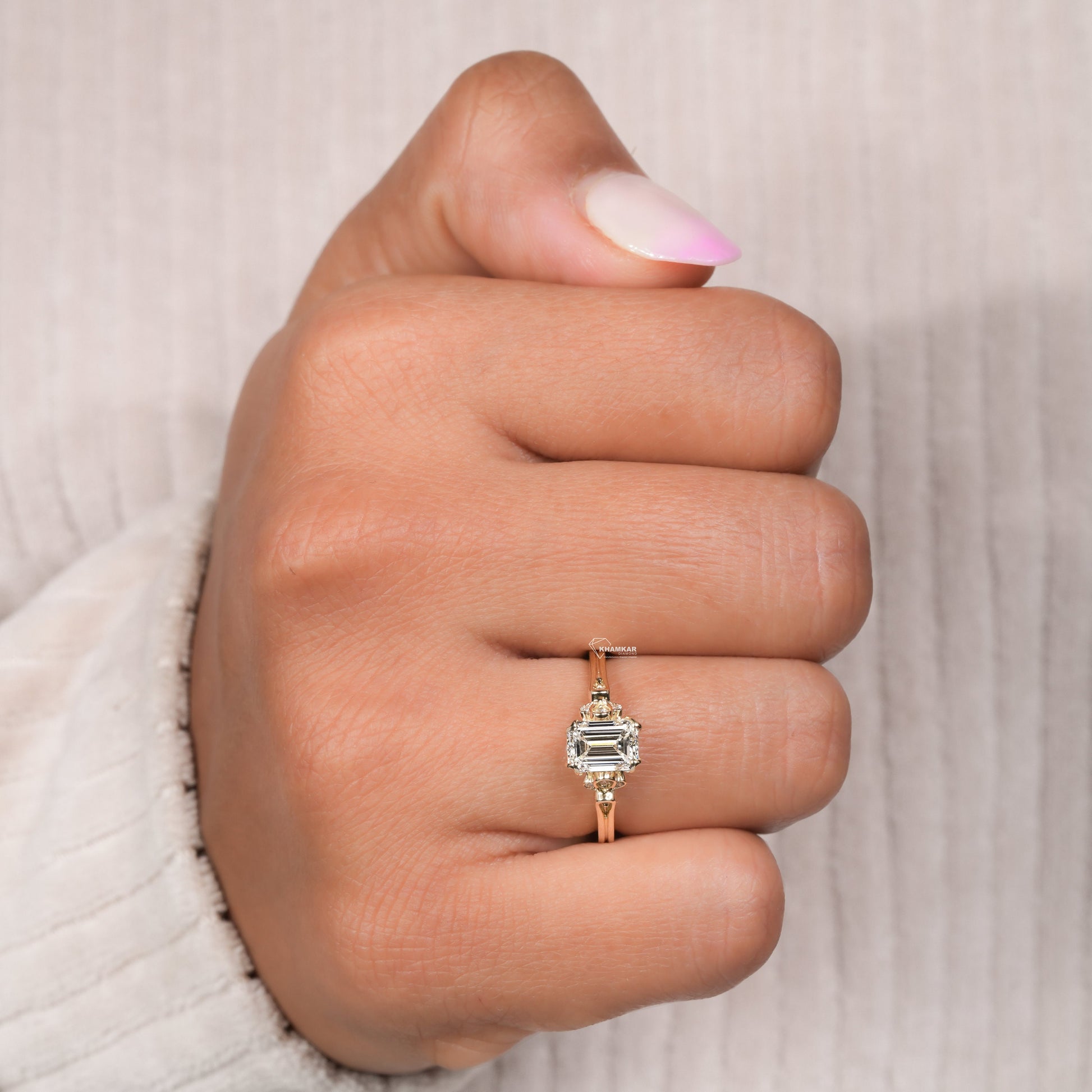 Engagement ring with rectangular clear gemstone, yellow metal band, halo design with round accent stones, worn on finger, top view
