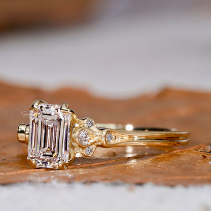 Engagement ring with rectangular clear gemstone, yellow metal band, leaf-inspired side accents with round stones, side profile view
