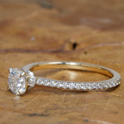 Engagement ring with round clear center stone, white metal pavé band, angled side profile view on wooden surface
