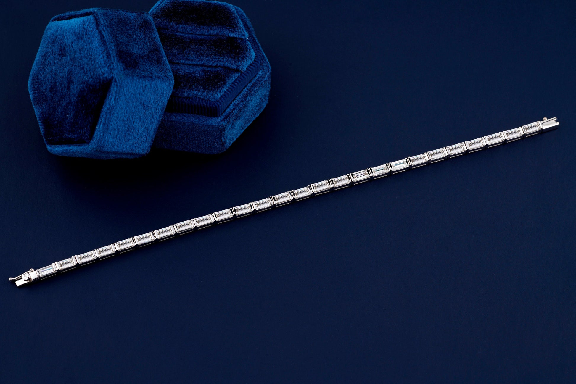 Bracelet with white metal links, rectangular step-cut stones in tennis bracelet design, full-length top view on a dark background
